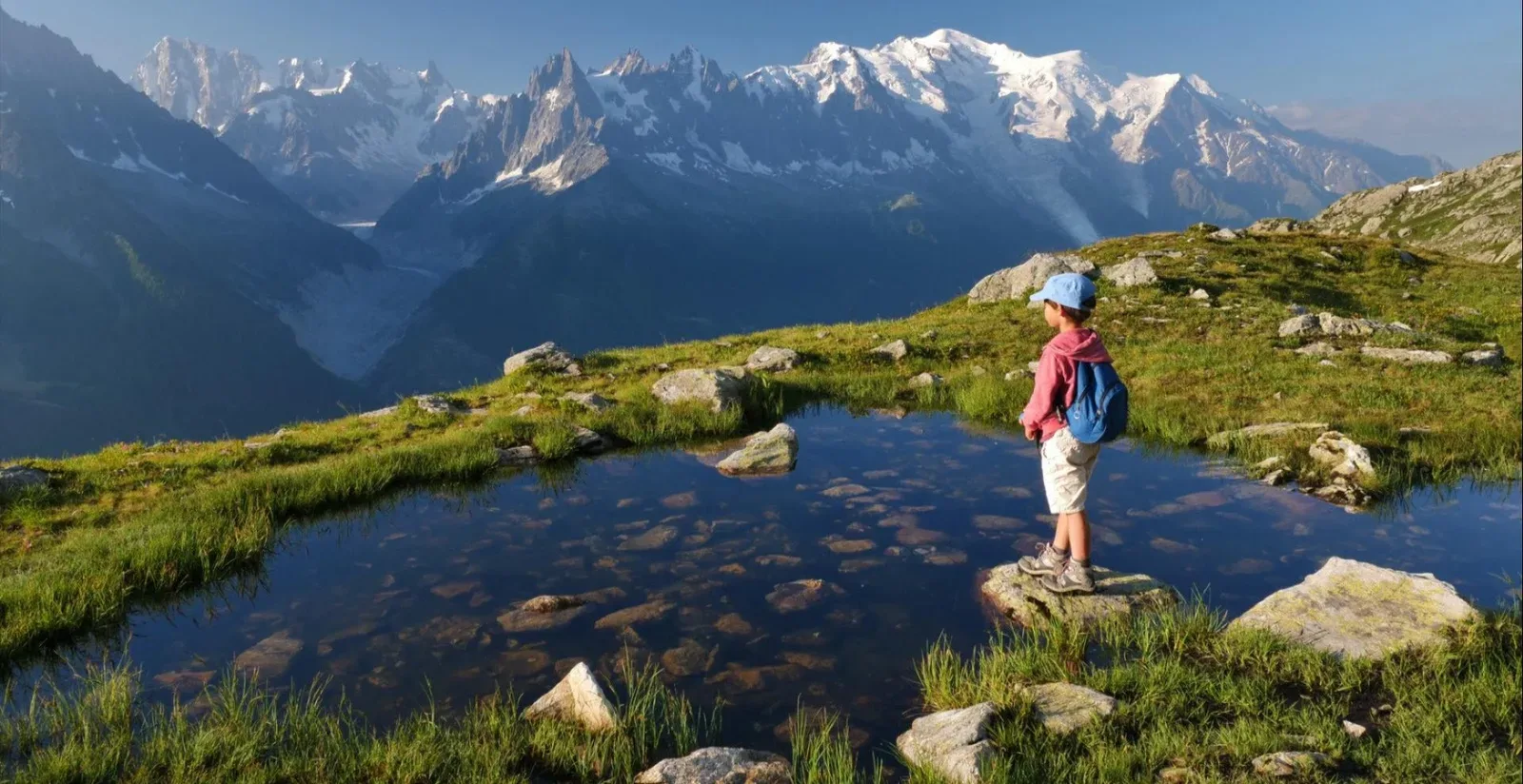 Un randonneur devant un lac d'altitude, face à la chaîne du Mont-Blanc